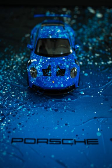 Modell eines blauen Porsche auf glitzerndem, blauen Untergrund.